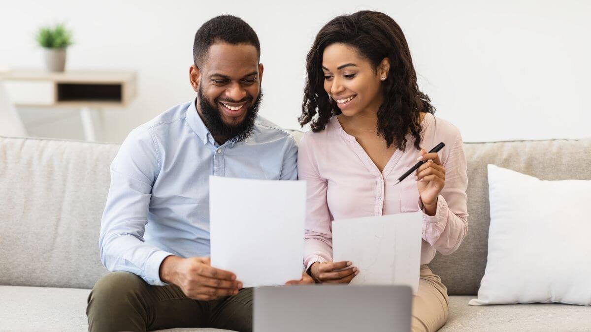 A couple sitting on a sofa smiling while reviewing documents together
