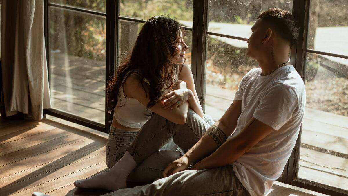 A couple sitting on the floor holding coffee mugs and having an open conversation