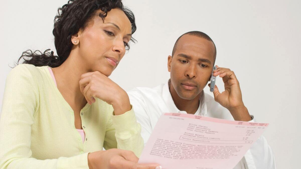 "A woman carefully reading a document while a man makes a phone call beside her