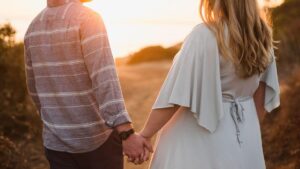 A couple holding hands and smiling at each other while walking through an autumn park